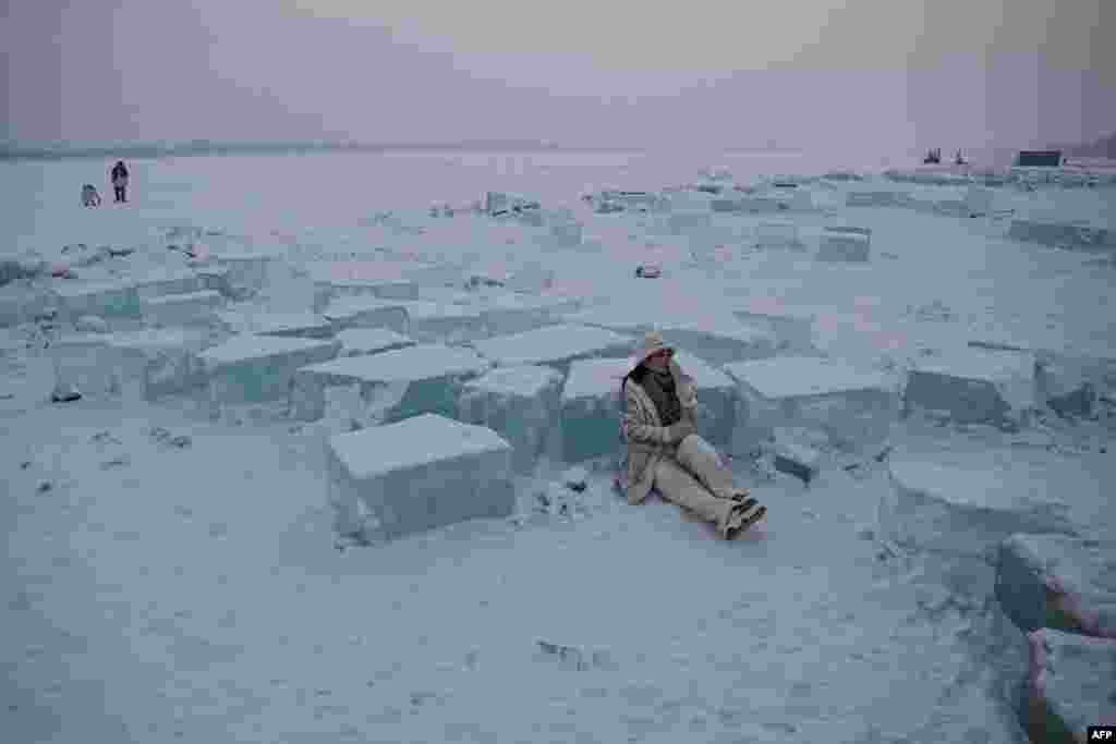 A woman poses beside blocks of cut ice on the frozen Songhua river in Harbin, in China's northeastern Heilongjiang province.