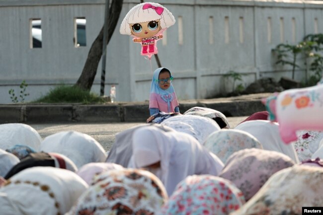 FOTO FILE: Gadis muslimah memegang balon saat mengikuti salat berjamaah Idulfitri di pelabuhan Sunda Kelapa, Jakarta, 2 Mei 2022. (REUTERS/Willy Kurniawan)