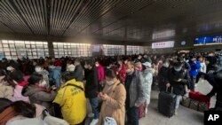 Antrean para pelancong yang mengenakan masker sambil membawa barang bawaan mereka, menunggu kedatangan kereta di Stasiun Kereta Api Barat di Beijing, Jumat, 6 Januari 2023. (AP/Wayne Zhang)