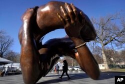 A passer-by walks under the 20-foot-high bronze sculpture "The Embrace," a memorial to Dr. Martin Luther King Jr. and Coretta Scott King, in the Boston Common, Jan. 10, 2023, in Boston.