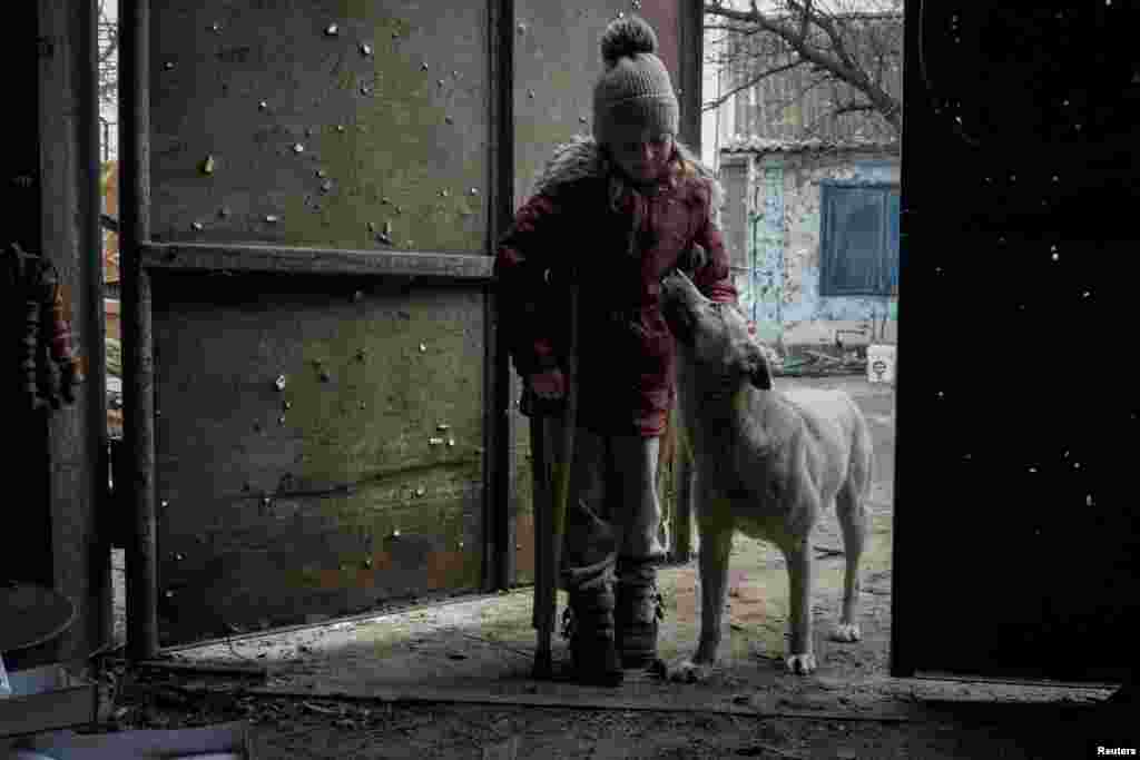 Local resident Zlata, 6, touches a dog at a gate with shrapnel holes near her house, in the village of Posad-Pokrovske, Kherson region, Ukraine, Dec. 7, 2022.
