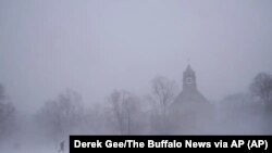 Un peatón con equipo para la nieve avanza por el Colonial Circle, con la silueta de la iglesia episcopaliana de St. John's Grace entre la ventisca, en Buffalo, Nueva York, el 24 de diciembre de 2022.