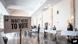 FILE - Polling location workers await a rush of lunchtime voters in the Georgia senate runoff election on Dec. 6, 2022, in Atlanta.