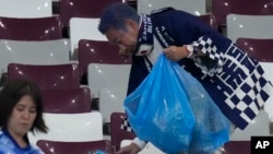 Para penggemar sepak bola asal Jepang membersihkan stadion usah laga antara Jepang dan Jerman di Stadion Internasional Khalifa di Doha, Qatar, Rabu, 23 November 2022. (Foto: Eugene Hoshiko/AP Photo)