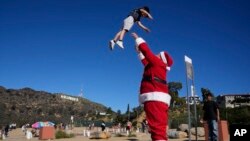 Brian Martinez mengenakan kostum Sinterklas, bermain dengan putranya, Braxon (4), di Lake Hollywood Park, Los Angeles, Sabtu, 24 Desember 2022. (AP/Damian Dovarganes)