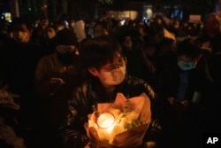 A protester holds flower and candles in Beijing, Sunday, Nov. 27, 2022. (AP Photo/Ng Han Guan)