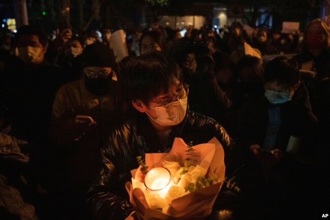 A protester holds flower and candles in Beijing, Sunday, Nov. 27, 2022. (AP Photo/Ng Han Guan)