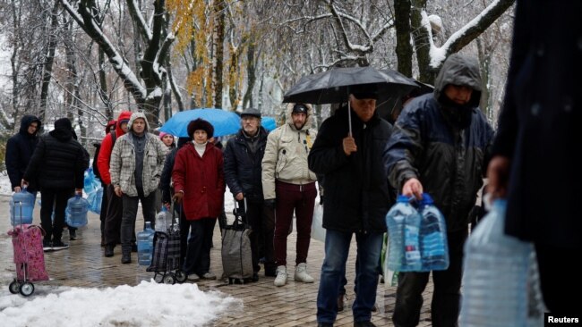 FILE - Local residents stand in line to fill up bottles with fresh drinking water after critical civil infrastructure was hit by Russian missile attacks in Kyiv, Nov. 24, 2022.