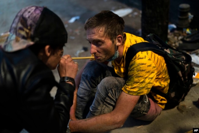 FILE - Homeless addicts Brandice Josey, left, uses a straw to blow a puff of fentanyl smoke into the mouth of Ryan Smith, who is high on the drug, in Los Angeles, Aug. 18, 2022.