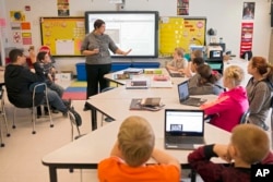 ComIn this photo taken Feb. 12, 2015, sixth grade teacher Carrie Young guides her students through an exercise on their laptops. (AP Photo/Ty Wright)