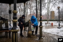 People collect water, in Kyiv, Nov. 24, 2022. Residents of Ukraine's bombed but undaunted capital clutched empty bottles in search of water and crowded into cafés for power and warmth Thursday.