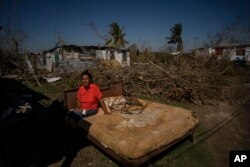 FILE - Mari Carmen Zambrano poses for a photo on her broken and wet bed as she dries it outside her home that lost its roof to Hurricane Ian in La Coloma, in the province of Pinar del Rio, Cuba, Oct. 5, 2022.