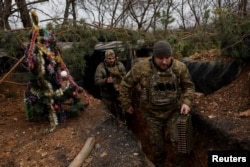 Ukrainian servicemen walk past a decorated Christmas tree in the trenches on the front line on Christmas Eve in Bakhmut, eastern Ukraine, Dec. 24, 2022.