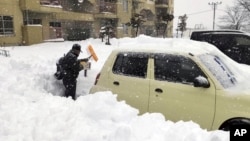 A resident shovels snow off around a car at a parking lot in Kitami city Hokkaido prefecture, northern Japan, on Dec. 24 2022.