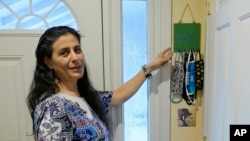 FILE -- Koloud "Kay" Tarapolsi points to a mask holder made by her daughter that has the phrase "To Your Health" written in Arabic on it, at her home in Redmond, Washington.