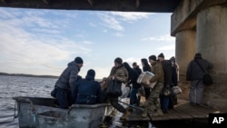 People get on a boat before crossing the Siverskyi-Donets river in front of a destroyed bridge in Staryi-Saltiv, Kharkiv region, Ukraine, Dec. 29, 2022.