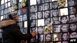FILE - In this file photo taken on January 8, 2022, a woman touches victims' portraits as mourners attend an outdoor vigil for the victims of Ukrainian passenger jet flight PS752, which was shot down two years ago over Iran, in Toronto, Ontario, Canada.