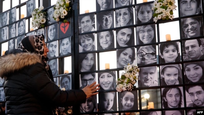 FILE - In this file photo taken on January 8, 2022, a woman touches victims' portraits as mourners attend an outdoor vigil for the victims of Ukrainian passenger jet flight PS752, which was shot down over Iran, in Toronto, Ontario, Canada.