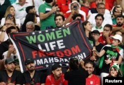 在伊朗對英格蘭的比賽賽場上，伊朗觀眾手舉印有抗議標語“女性、生命、自由”的抗議旗幟。（2022年11月21日）