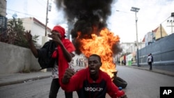 Manifestantes gritan consignas contra el gobierno frente a una barricada de neumáticos en llamas durante una protesta, el viernes 18 de noviembre de 2022, en Puerto Príncipe, Haití. 