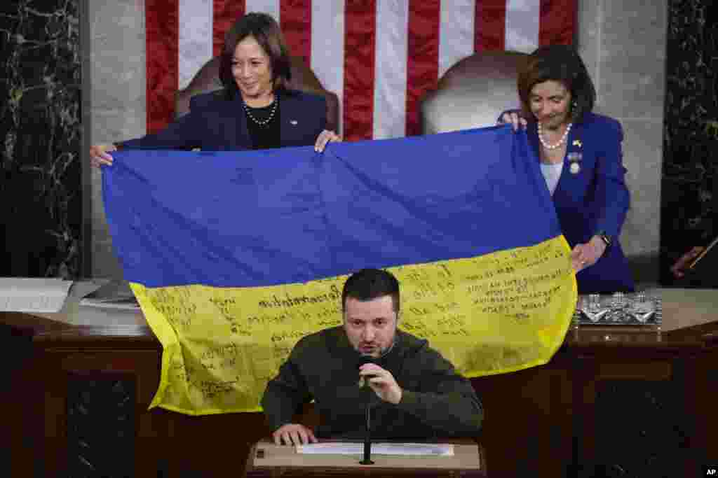 U.S. Vice President Kamala Harris and House Speaker Nancy Pelosi of Calif., right, react as Ukrainian President Volodymyr Zelenskyy presents lawmakers with a Ukrainian flag autographed by front-line troops in Bakhmut, in Ukraine&#39;s contested Donetsk province, as he addresses a joint meeting of Congress on Capitol Hill in Washington, Dec. 21, 2022.