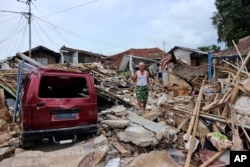 Seorang pria berjalan di atas puing-puing rumah di lingkungan yang terdampak gempa yang parah di Cianjur, Jawa Barat, Jumat, 25 November 2022. Gempa berkekuatan 5,6 itu menewaskan ratusan orang, banyak di antaranya anak-anak, dan melukai ribuan lainnya. (AP Photo/Rangga Firmansyah)