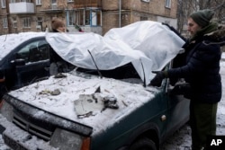 A couple cover their damaged car with a plastic tarp after a Russian attack in Kyiv, Ukraine, Wednesday, Dec. 14, 2022. (AP Photo/Evgeniy Maloletka)