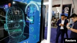 FILE - Visitors check their phones behind a screen advertising facial recognition software during the Global Mobile Internet Conference at the National Convention in Beijing, April 27, 2018.