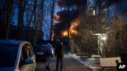 Residents watch at a burning infrastructure project hit during a massive Russian drone night strike in Kyiv, Ukraine, Dec. 19, 2022. 