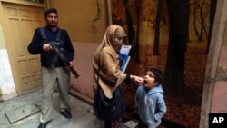 FILE - A police officer stands guard while a health worker gives a polio vaccine to a child in Peshawar, Pakistan, Dec. 5, 2022.