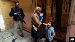 Seorang petugas polisi berjaga saat petugas kesehatan memberikan vaksin polio kepada seorang anak di Peshawar, Pakistan (foto: dok). 