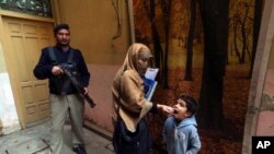 FILE - A police officer stands guard while a health worker gives a polio vaccine to a child in Peshawar, Pakistan, Dec. 5, 2022.