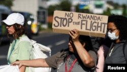 An activist blocking a road leading away from the Colnbrook Immigration Removal Centre holds a banner during a protest against the British Governments plans to deport asylum seekers to Rwanda, near Heathrow airport in London, June 14, 2022.