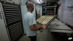 Baker David Buelens carries uncooked baguettes to the oven at a bakery in Versailles, west of Paris, Nov. 29, 2022.