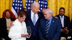 Gladys Sicknick, mother of the late U.S. Capitol Police Officer Brian Sicknick, holds the medal President Joe Biden awarded to her son, at a White House ceremony Jan. 6, 2023, marking the anniversary of the assault on the Capitol. Sicknick's father Charles is at right. 