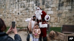 Issa Kassissieh dresses as Santa Claus to pose for photos with children and a camel in Jerusalem, Dec. 23, 2021.