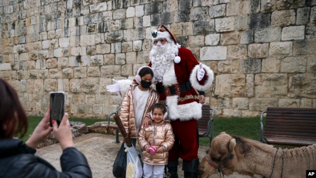 Issa Kassissieh dresses as Santa Claus to pose for photos with children and a camel in Jerusalem, Dec. 23, 2021.