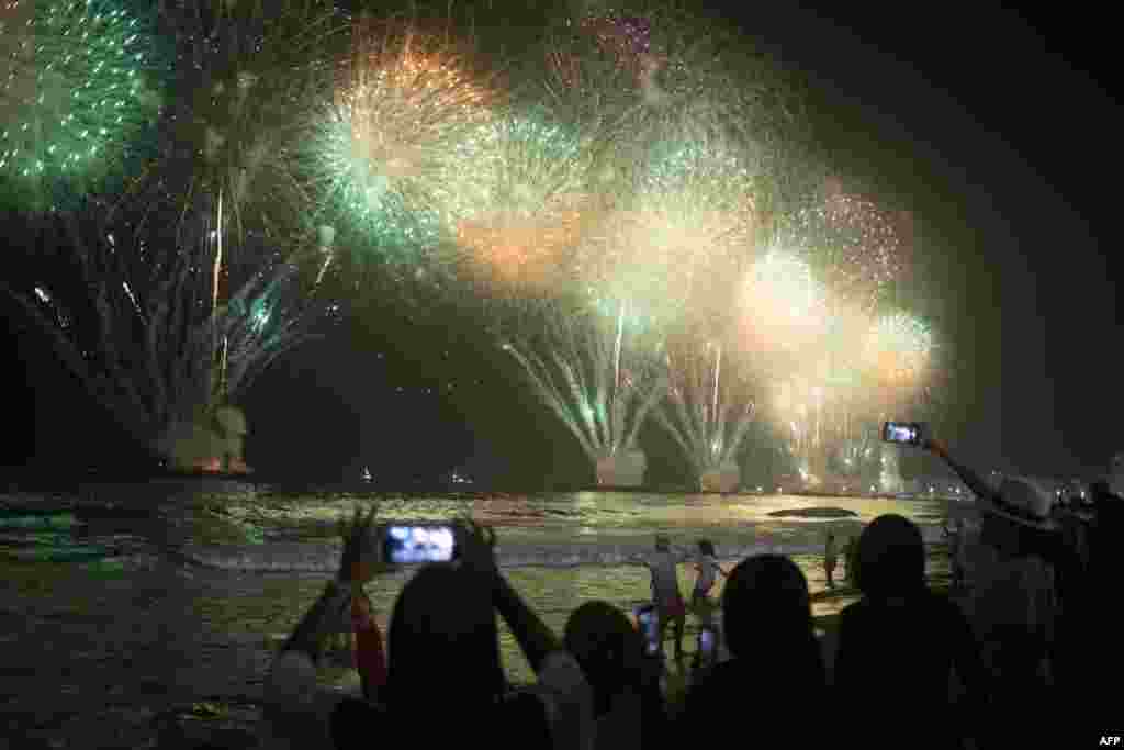 La gente celebra mientras los tradicionales fuegos artificiales de Año Nuevo iluminan el cielo en la playa de Copacabana en Río de Janeiro, Brasil, el 1 de enero de 2023. [AFP]