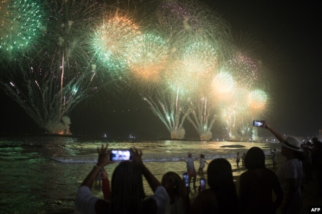 La gente celebra mientras los tradicionales fuegos artificiales de Año Nuevo iluminan el cielo en la playa de Copacabana en Río de Janeiro, Brasil, el 1 de enero de 2023. [AFP]