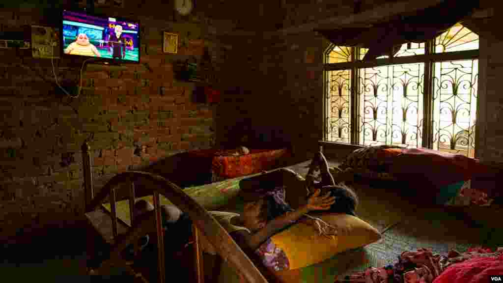 The sons of Urmila Sah watch TV in the house her late husband built with the money he made working in Qatar before he died, pictured in the Dhanusha district of Nepal, August 2022 (Yan Boechat/VOA)