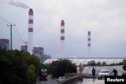 Pria berdiri di dekat mobil di dekat pembangkit listrik tenaga batu bara di Shanghai, China, 21 Oktober 2021. (Foto: REUTERS/Aly Song)