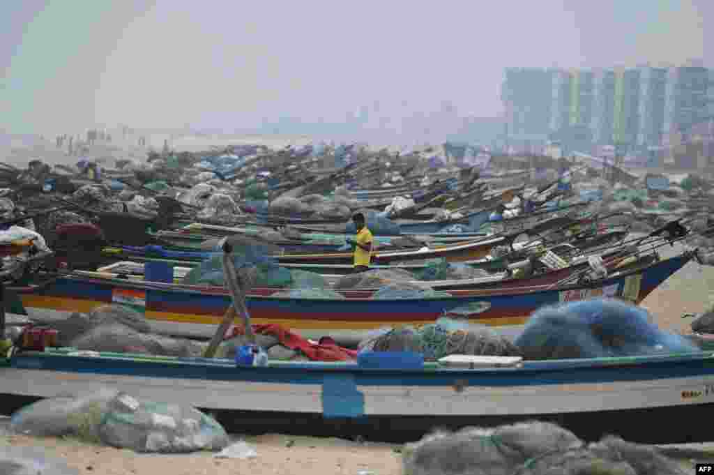 A man walks past fishing boats at Marina beach at Marina beach in Chennai, India, during preparations ahead of Cyclone Mandous landfall in north Tamil Nadu-south Andhra Pradesh coasts.