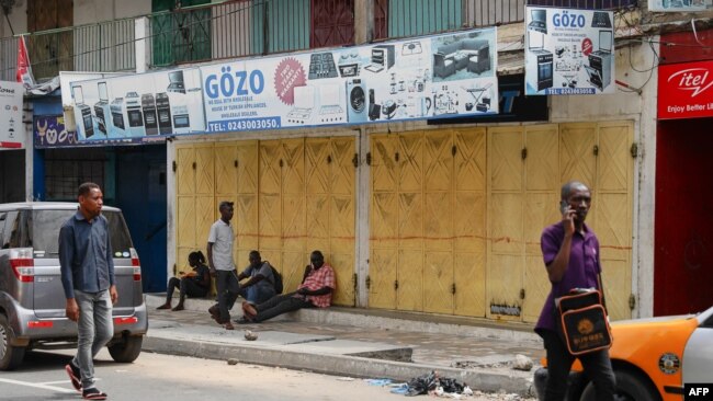 FILE - People sit in front of closed shops in the central business area of Accra, after shop owners in Ghana's capital closed their shops in protest of high costs, on Oct. 20, 2022.