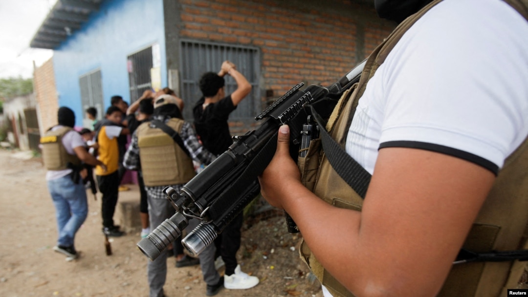 FILE - A member of Honduras' Police Anti Maras and Gangs Against Organized Crime Directorate stands guard as other directorate members frisk people in Tegucigalpa, Honduras, Nov. 26, 2022. 