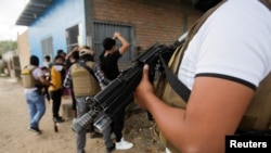 Seorang anggota polisi dari Direktorat Antigeng dan Kejahatan Terorganisasi Honduras berjaga, sedangkan rekannya memeriksa sejumlah orang di Tegucigalpa, Honduras, 26 November 2022. (Foto: Fredy Rodriguez/Reuters)