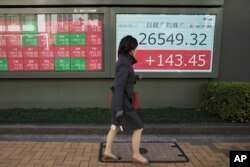 Seorang perempuan berjalan melewati monitor yang menunjukkan indeks Nikkei 225 Jepang di sebuah perusahaan sekuritas di Tokyo, Selasa, 27 Desember 2022. (AP /Hiro Komae) gambar