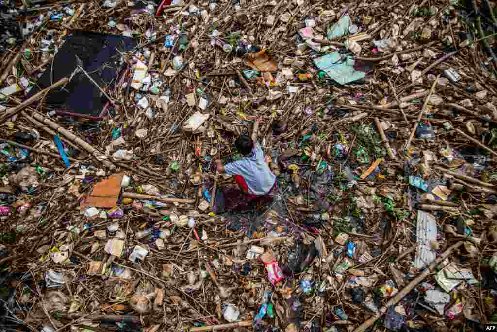 A boy plays on a drain covered with household waste in Bogor, Indonesia.