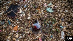A boy plays on a drain covered with household waste in Bogor, Indonesia.