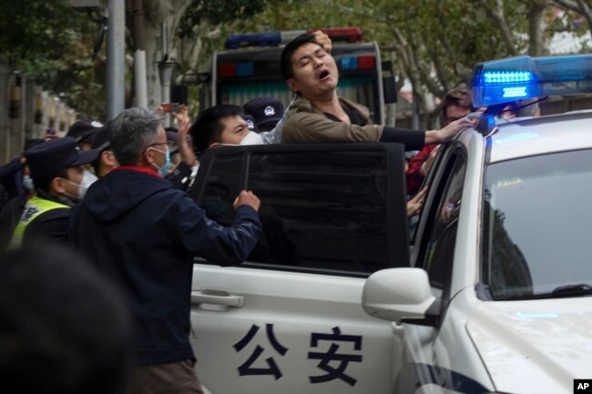 In this photo taken on Sunday, Nov. 27, 2022, a protester reacts as he is arrested by policemen during a protest on a street in Shanghai, China. (AP Photo)