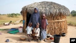 FILE - Aisha Ali, 40, stands with her children outside the hut where she found refuge from the floods in Darayami, northeastern Nigeria, Oct. 26, 2022. 